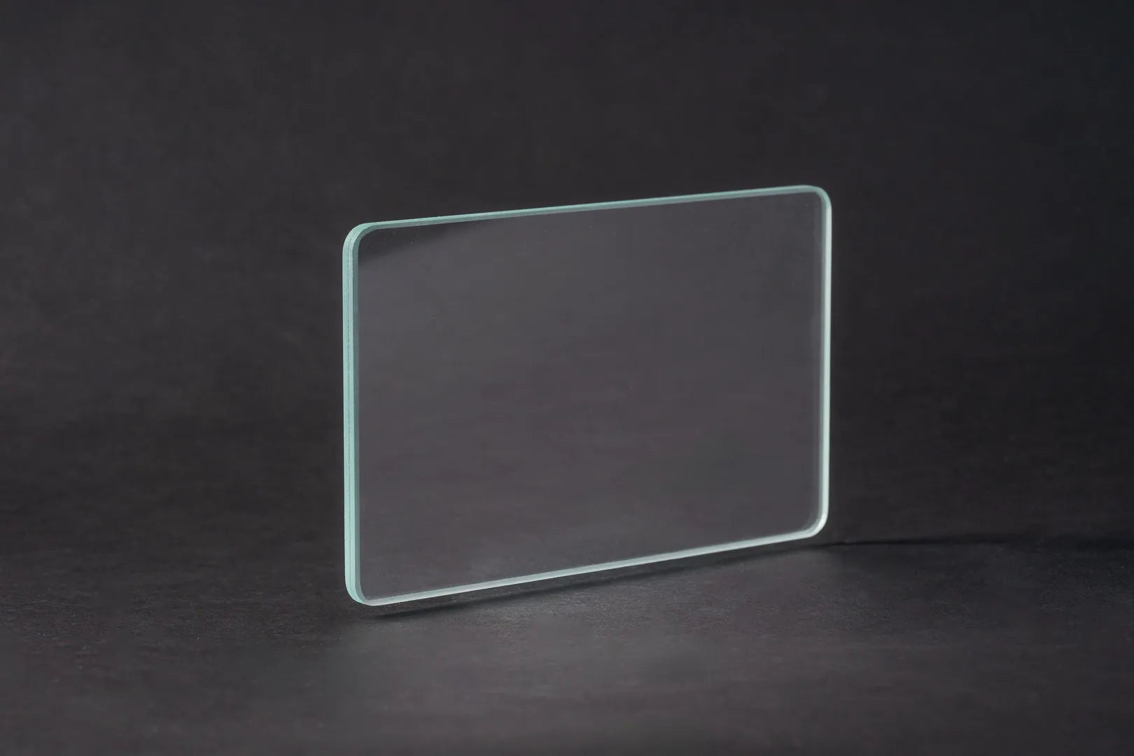 Eine rechteckige Scheibe aus Entspiegeltes Glas steht aufrecht vor einem dunklen, schlichten Hintergrund, dessen Kanten durch Lichtreflexion subtil hervorgehoben werden.