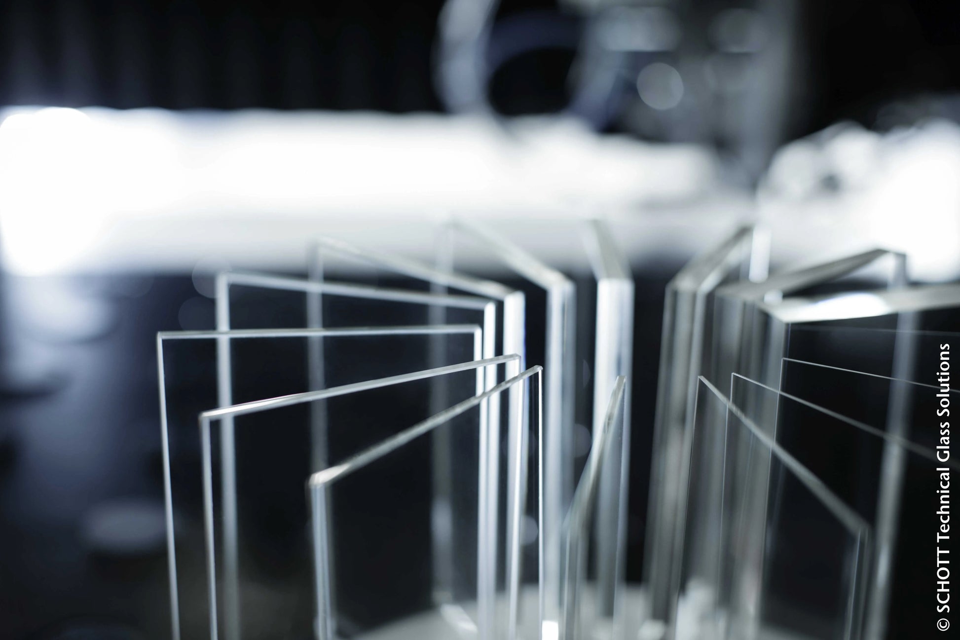 Nahaufnahme mehrerer hochtemperaturbeständiger Glasscheiben, die aufrecht in einer Reihe stehen, mit einem unscharfen Hintergrund und einer hellen Lichtquelle dahinter. Bildnachweis: SCHOTT Technical Glass Solutions.