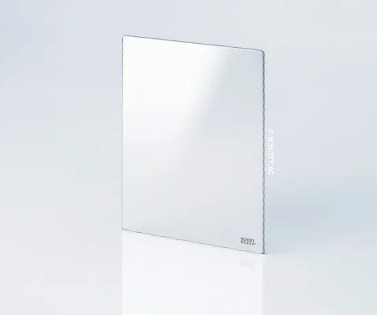 Ein rechteckiger, rahmenloser Spiegel aus hochtemperaturbeständigem Glas steht aufrecht auf einer weißen Fläche mit einer schwachen Reflexion. Der Hintergrund ist einfarbig und hell gefärbt.