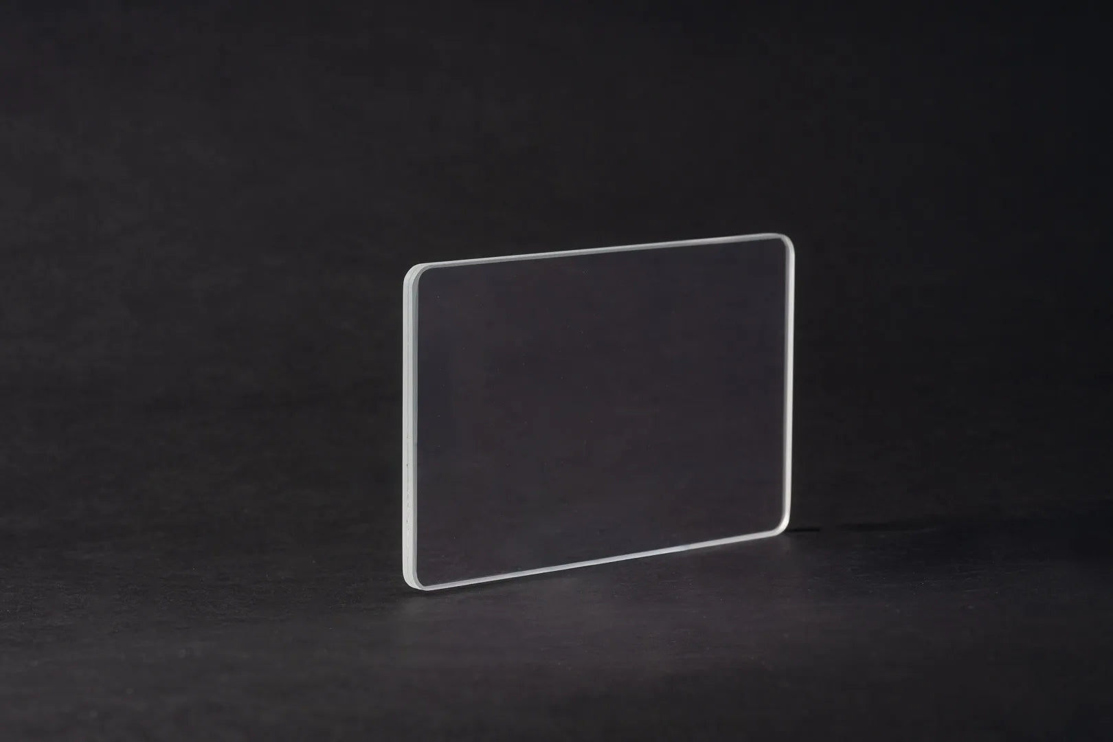 Eine einzelne, klare Platte aus Entspiegeltes Glas steht aufrecht auf einer dunklen, glatten Oberfläche vor einem schwarzen Hintergrund.